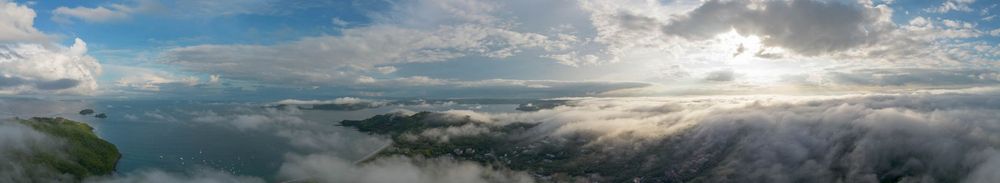 Aerial panoramic view of a stunning cloudscape over a lush green landscape at sunset with dramatic sky.