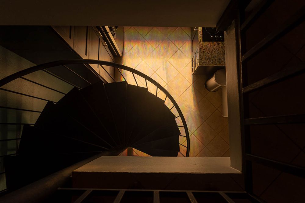 Dramatic overhead view of an elegant spiral staircase with warm golden lighting and decorative wallpaper in a luxury interior.