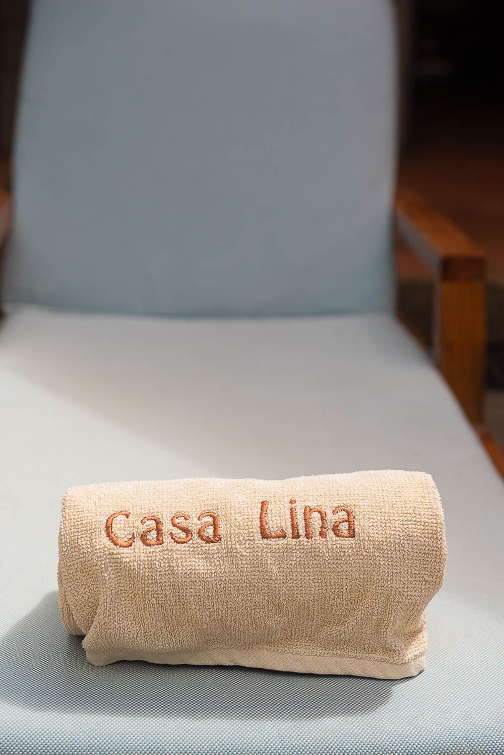 A rolled burlap bag embroidered with Casa Lina resting on a light blue chair cushion.