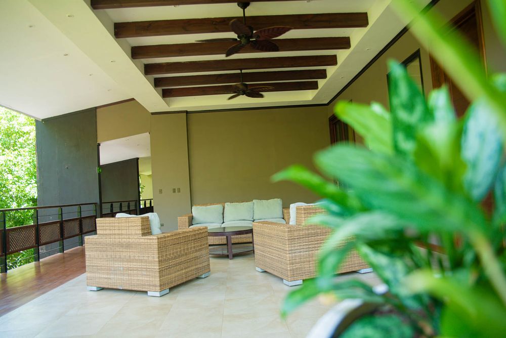 Elegant covered patio with wicker furniture, ceiling fan, and lush tropical greenery in a luxury outdoor living space.