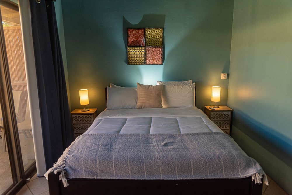 Cozy bedroom with a queen bed, teal walls, matching nightstand lamps, and colorful wall art.