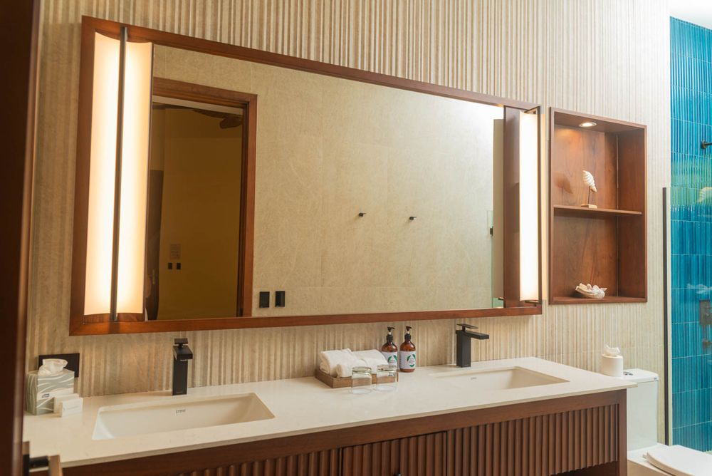 Modern double sink bathroom vanity with large wood-framed mirror, lit side panels, and open shelving with teal tile accent.