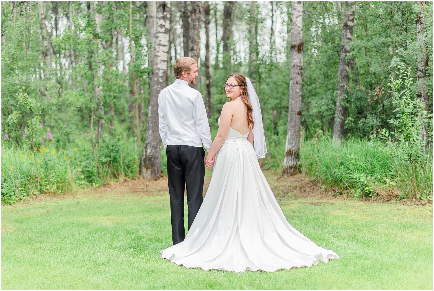 Bride and groom holding hands facing a birch tree forest in wedding attire.
