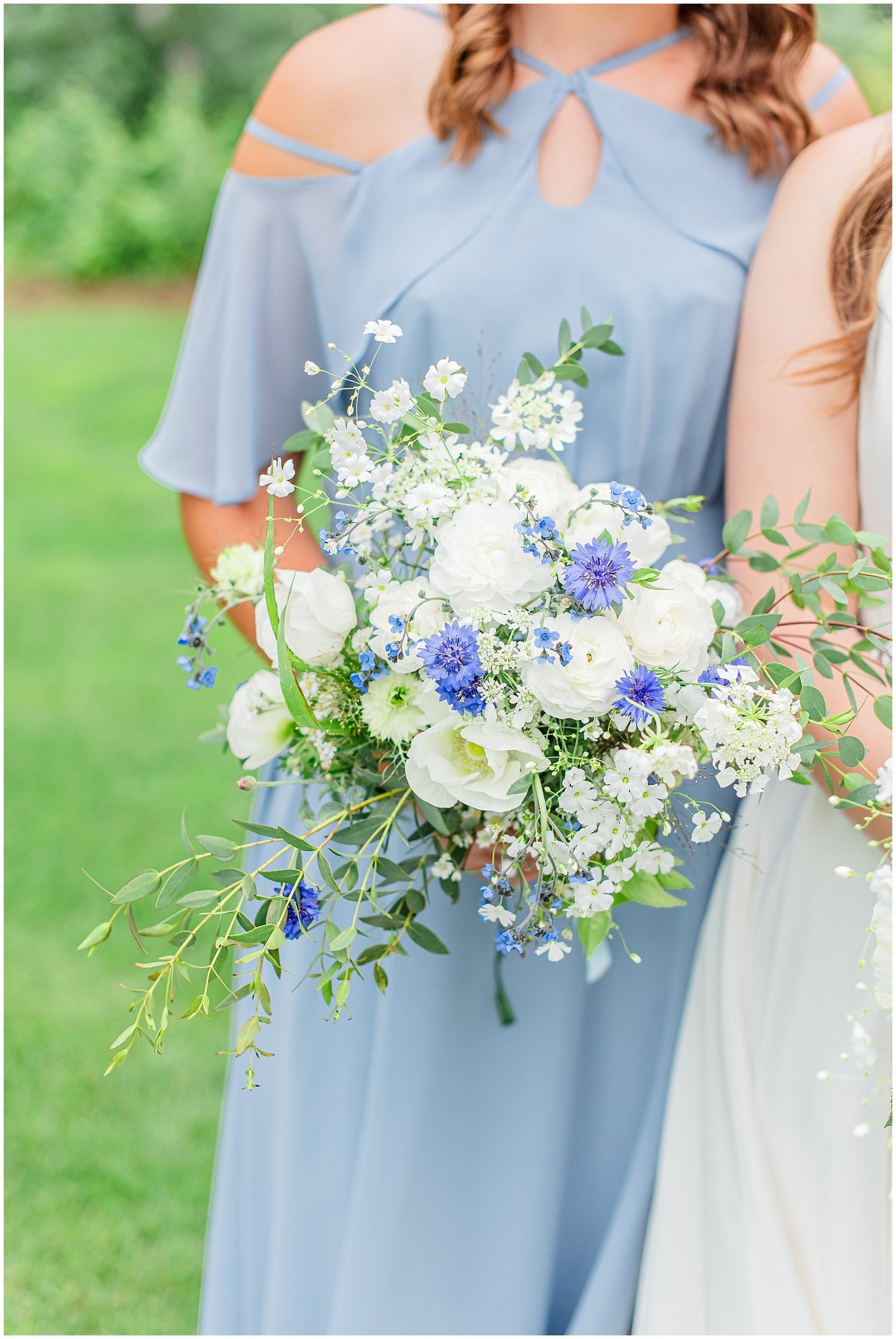 Bridesmaid in dusty blue dress holding a white and blue floral wedding bouquet.