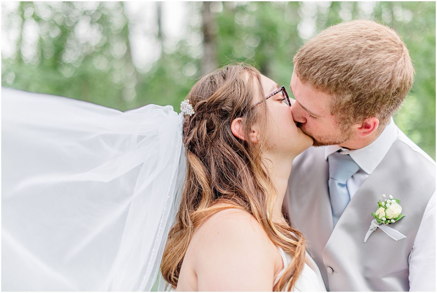 Bride and groom share a kiss as her veil flows in the breeze outdoors.