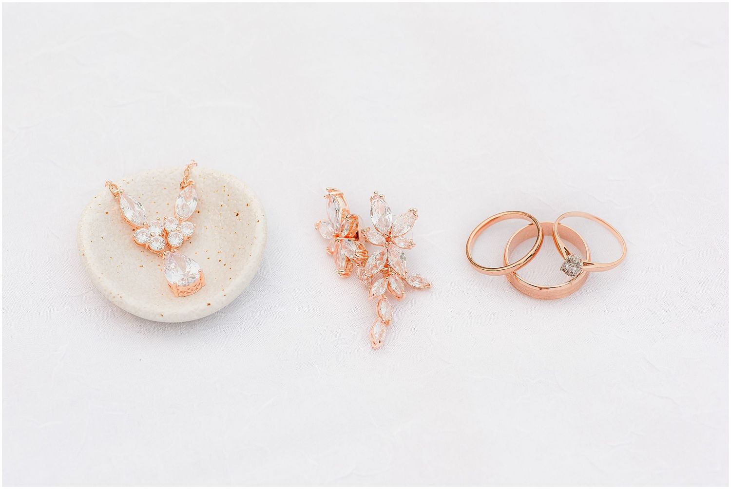 Rose gold butterfly earrings, floral brooch, and stacking rings arranged on white stone jewelry dish.