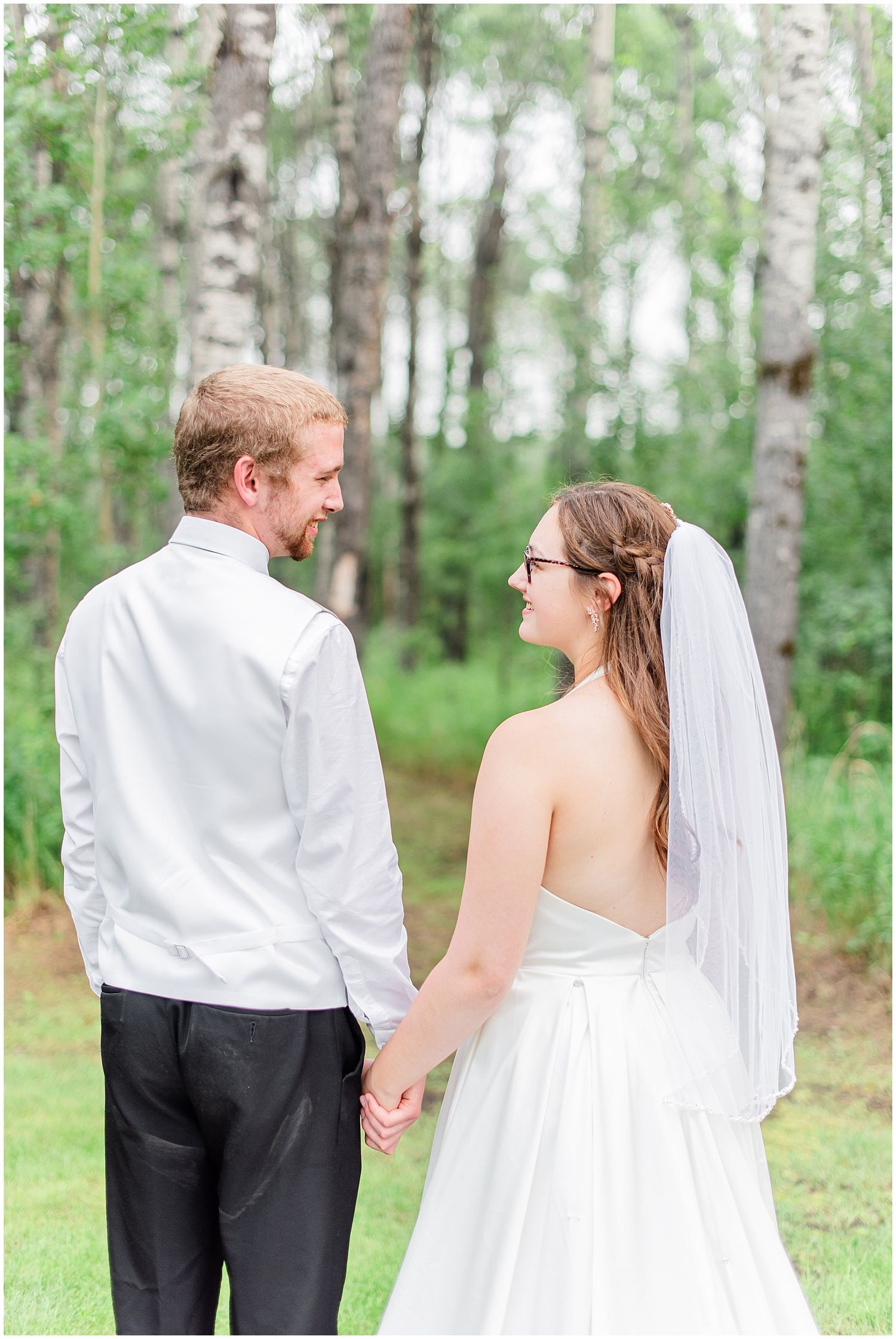 Bride and groom holding hands facing each other in front of birch trees on their wedding day.