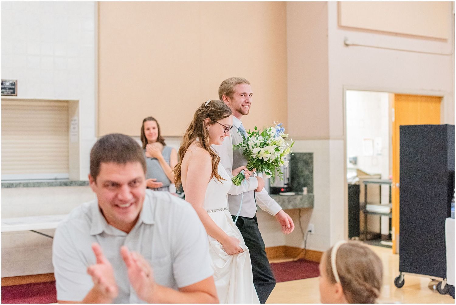 Bride and groom enter their wedding reception hall as guests applaud and celebrate their arrival.