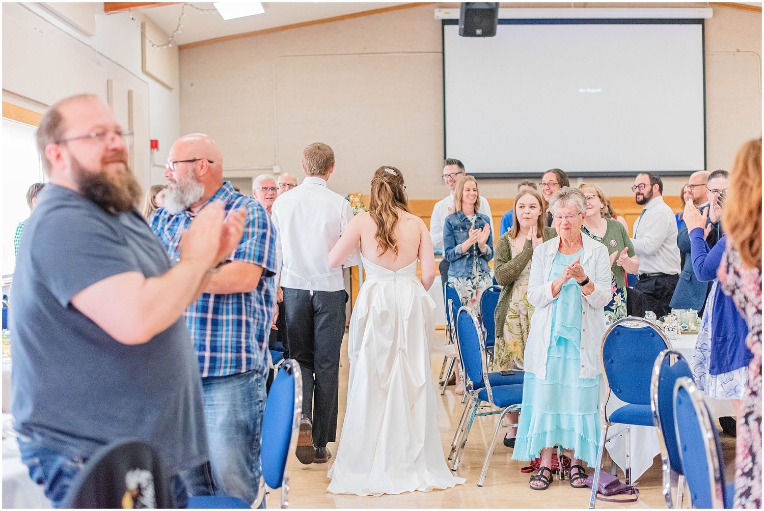 Wedding guests applaud as bride and groom enter their reception hall in a warm celebratory welcome.