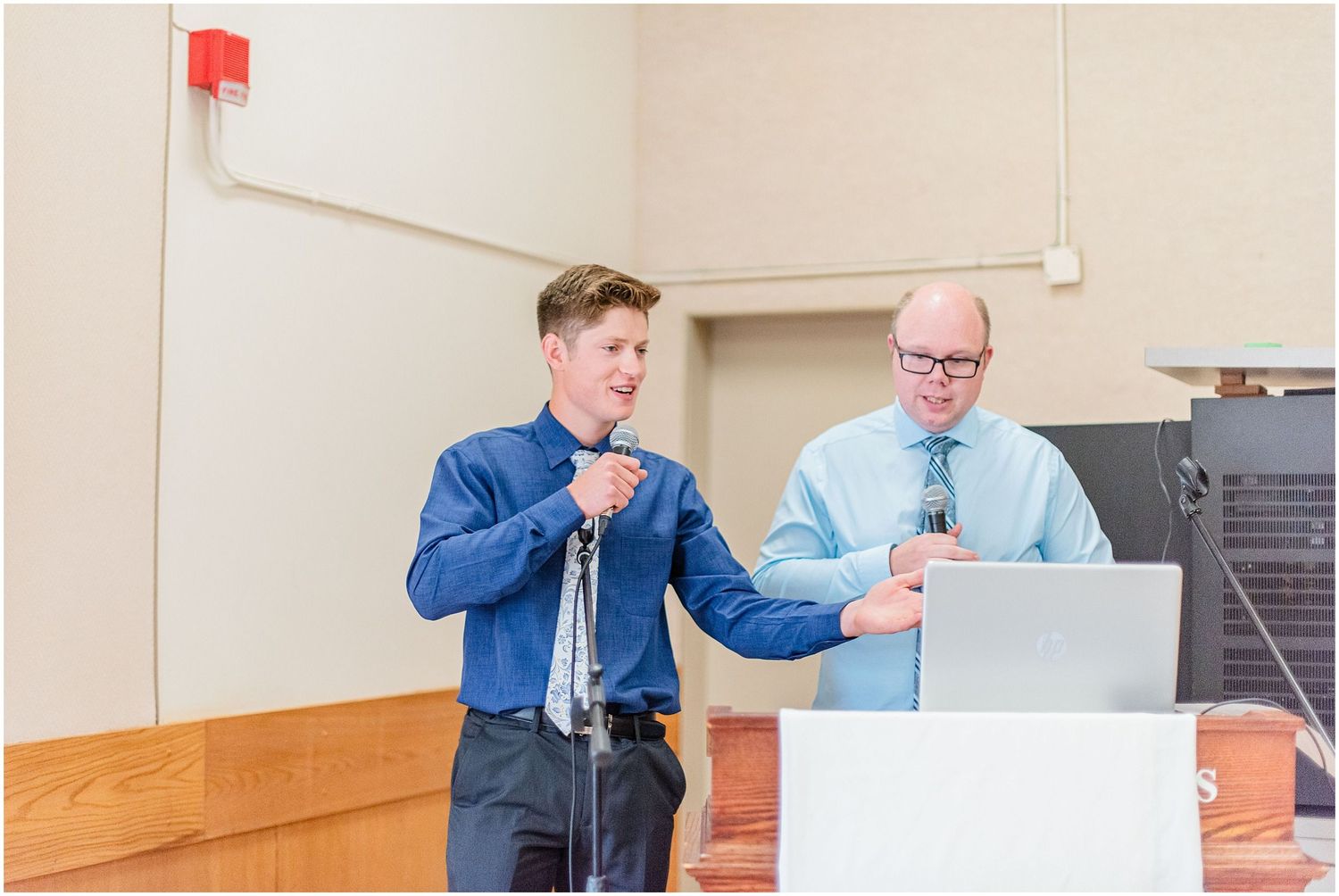 Two men presenting at podium with microphone and laptop during indoor event or ceremony.