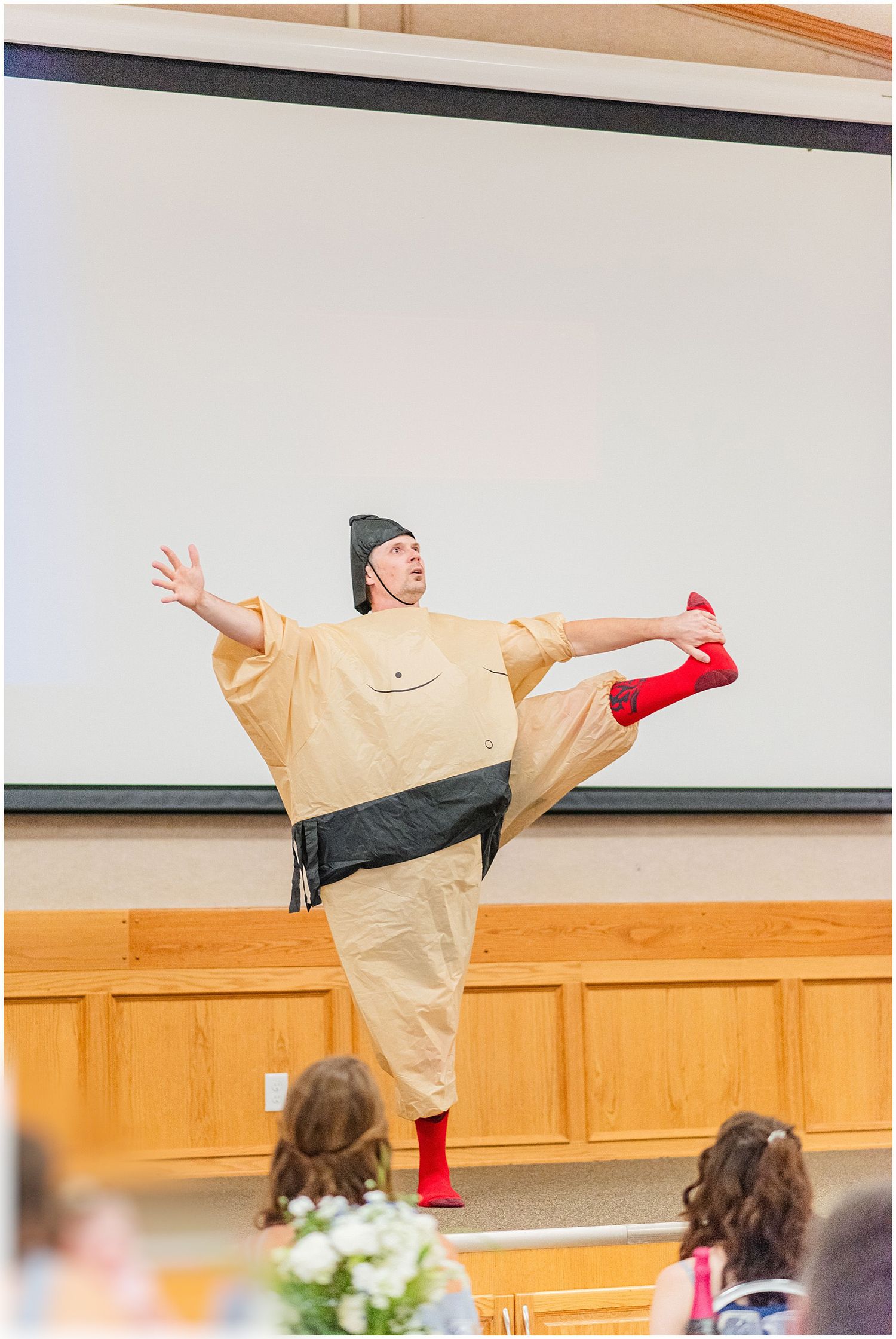 Person performing in a sumo wrestler costume with red socks at a wedding reception.
