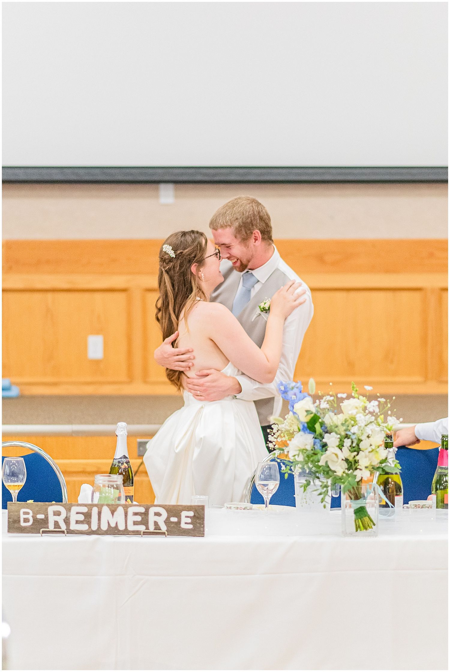 Newlyweds share a kiss at sweetheart table with B-REIMER-E sign at reception.