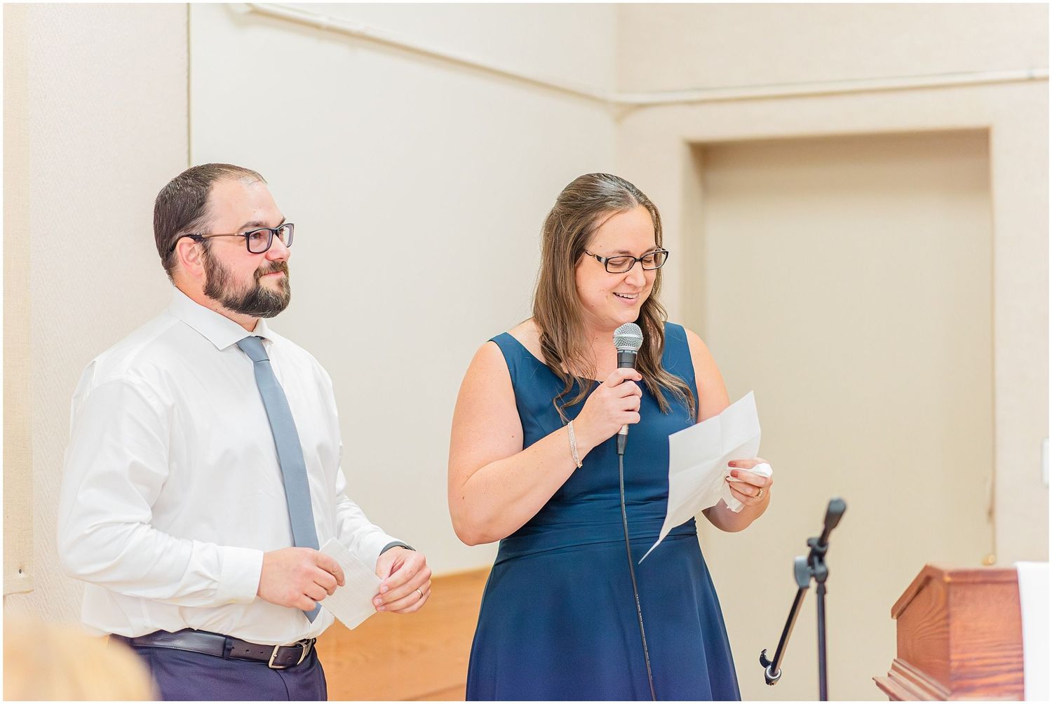 Man and woman in formal attire giving speech with microphone at indoor event.