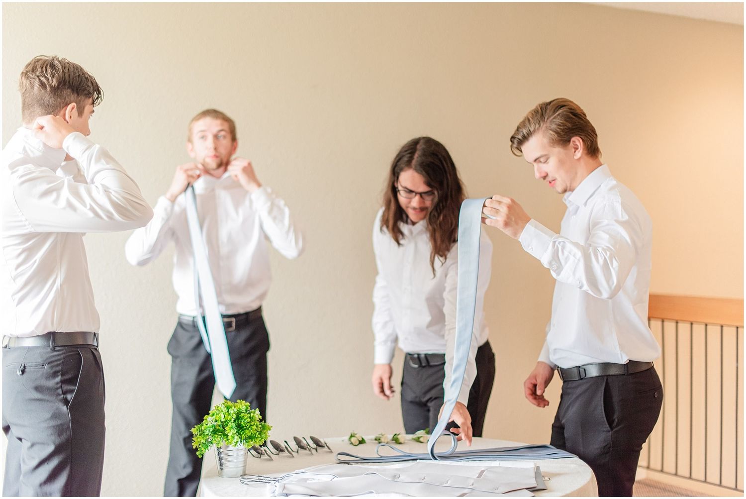 Groomsmen in white shirts practice tying neckties before a wedding ceremony at an elegant venue.