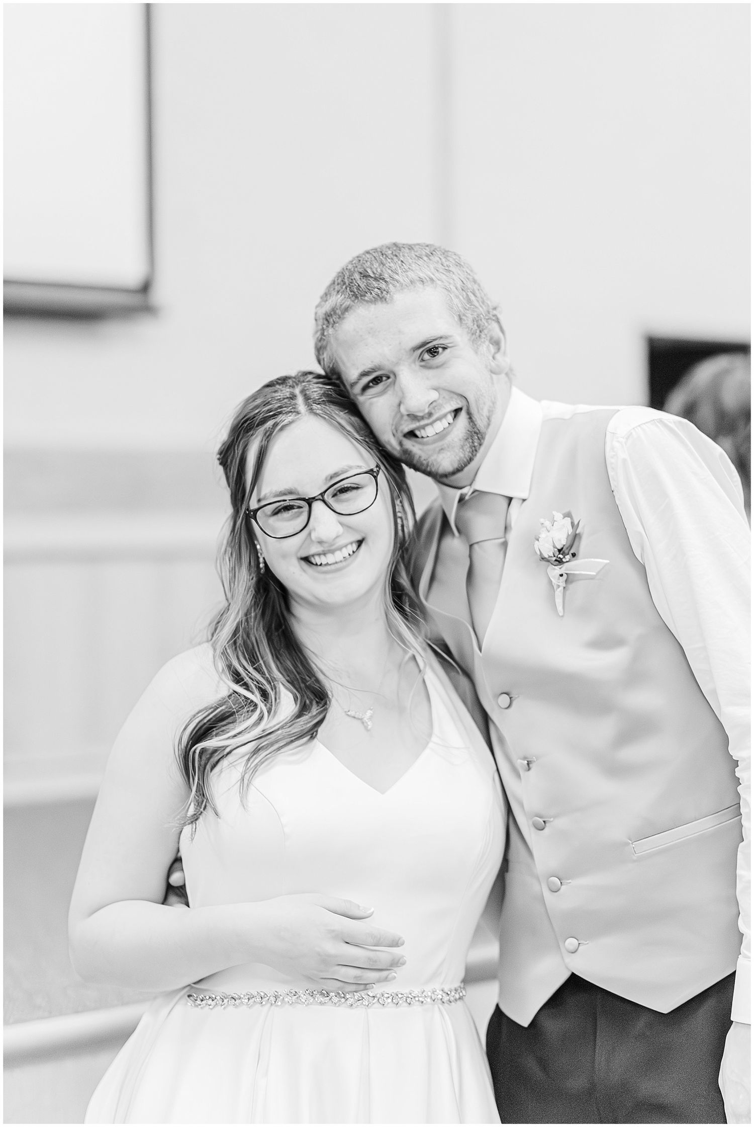 Black and white photo of a smiling bride and groom posing together at their wedding reception.
