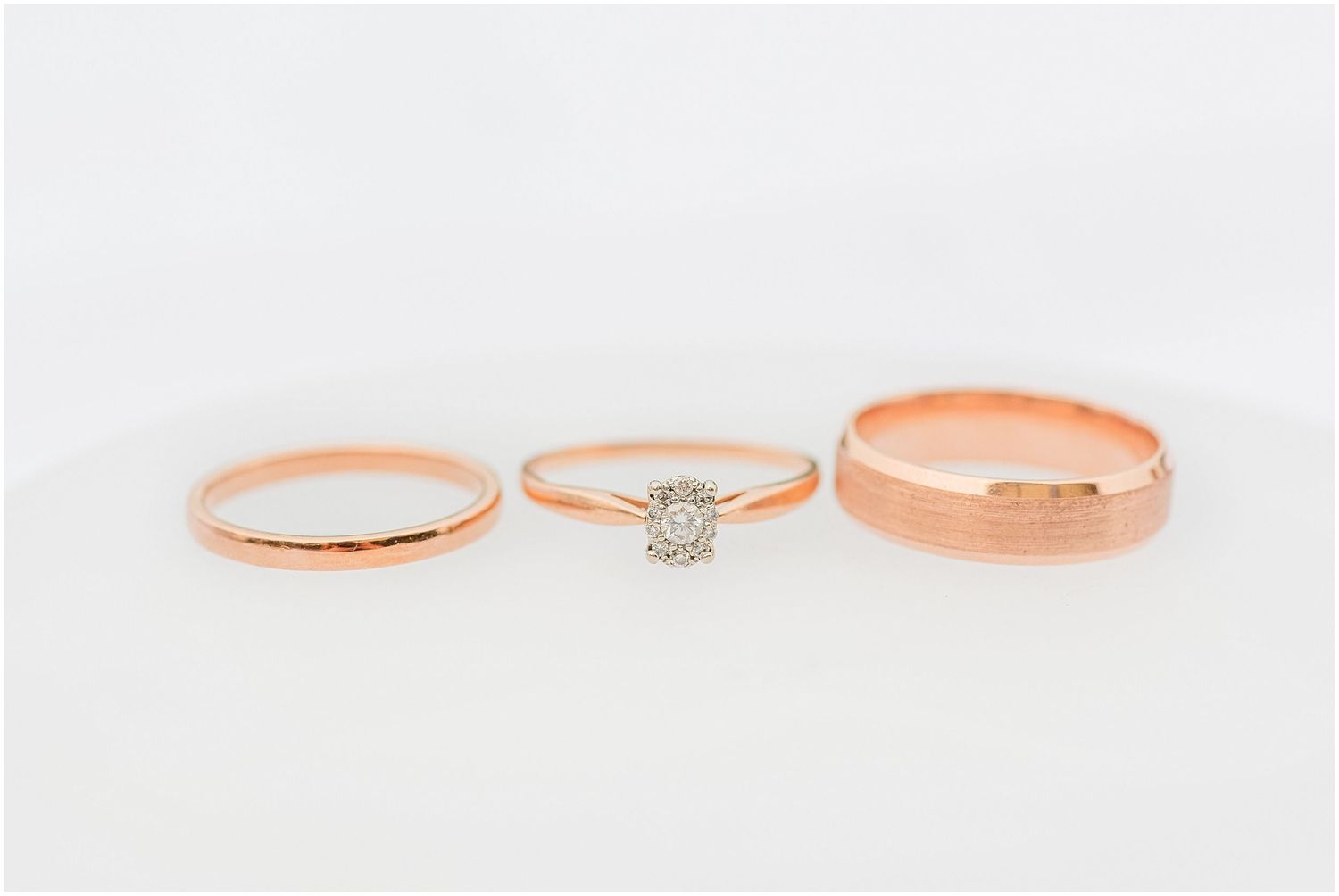 Three rose gold rings displayed on white background, including two bands and a diamond halo engagement ring.