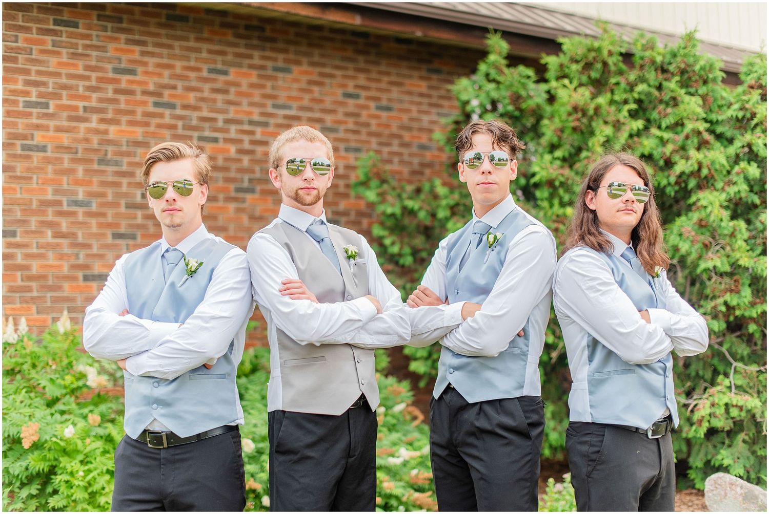 Four groomsmen in light blue vests and sunglasses posing confidently outdoors before a wedding.