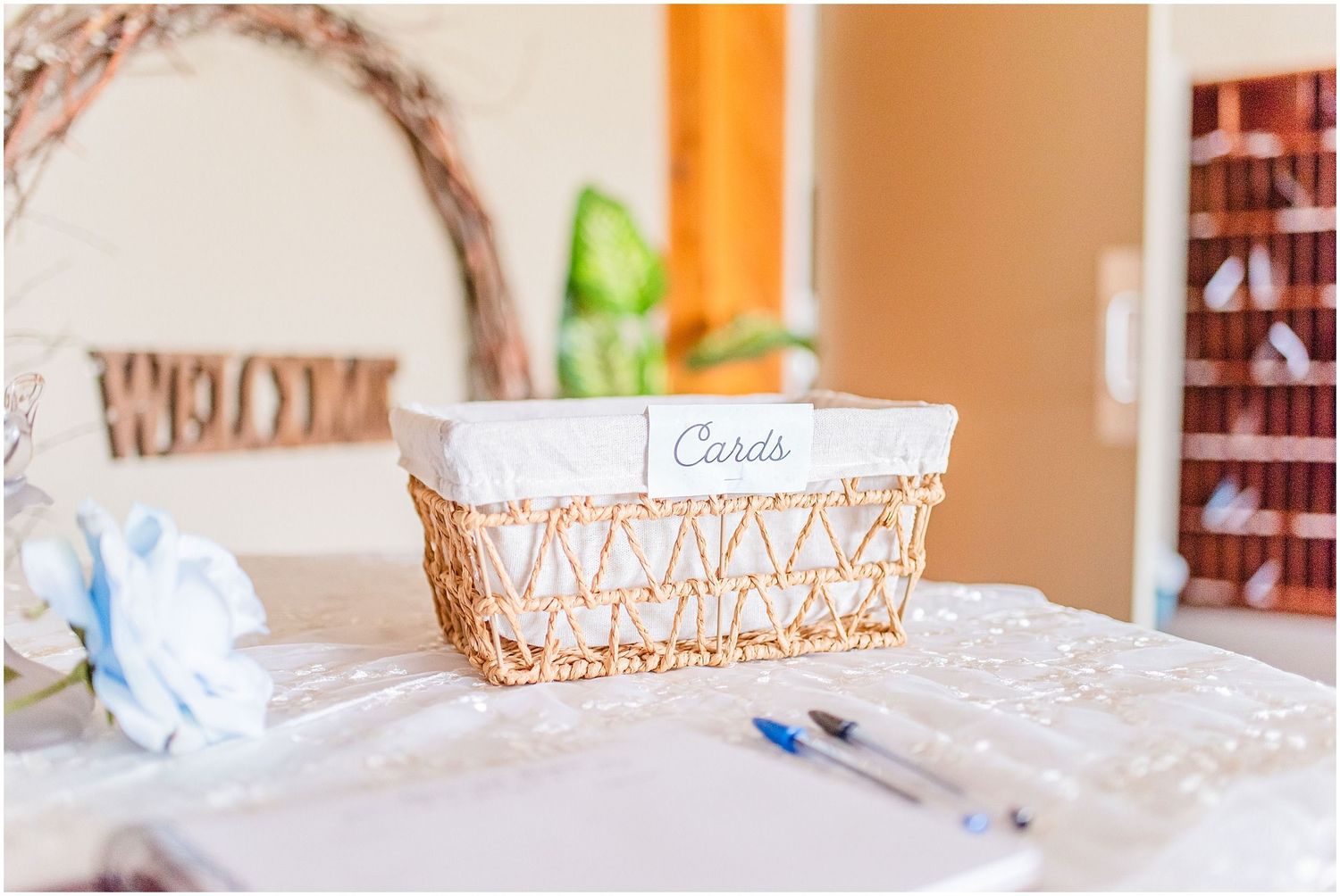A wicker basket labeled Cards sits on a lace-covered table at a wedding reception venue.