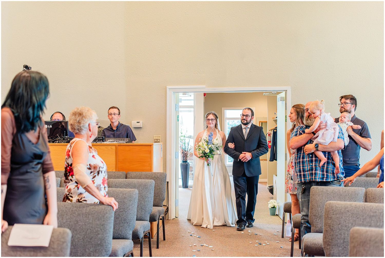 Bride walking down the aisle with escort at an elegant wedding ceremony venue with gray chairs.