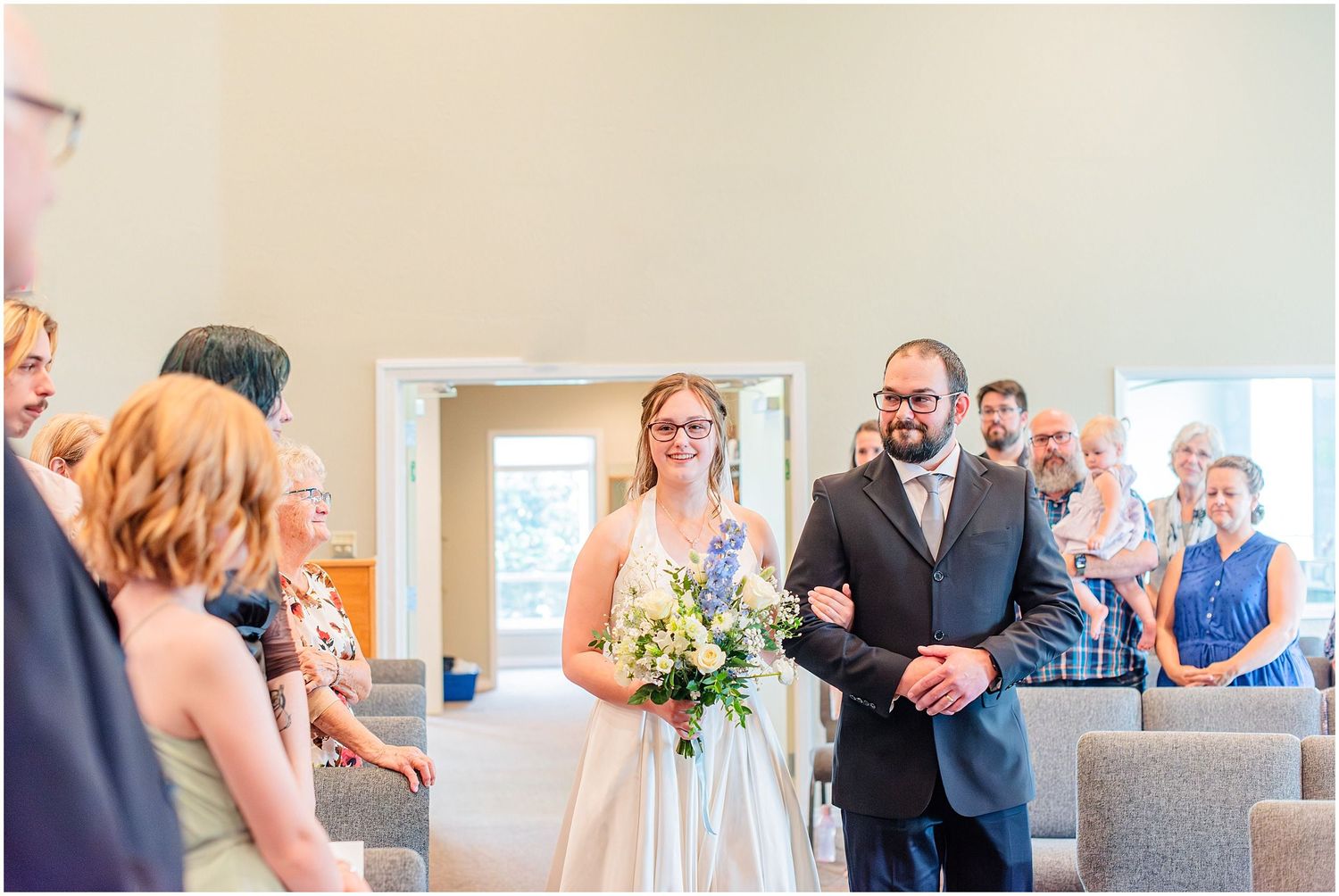 Bride with bouquet walks down church aisle escorted by father during wedding ceremony.
