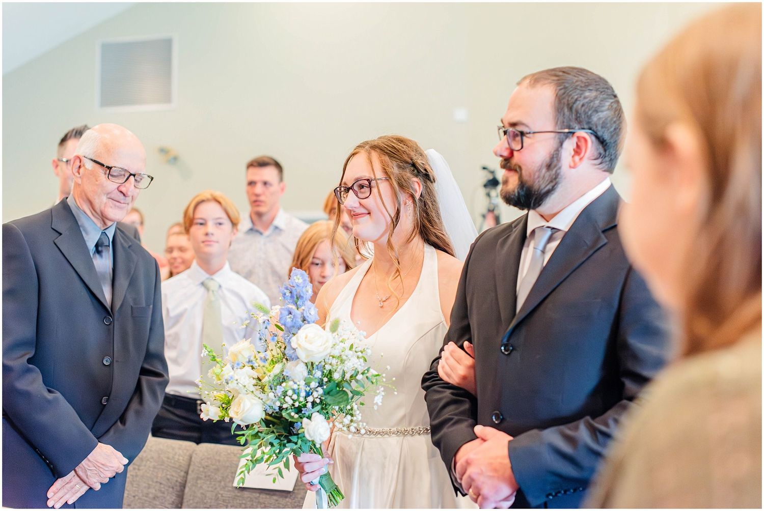 Bride and groom walking down aisle holding blue and white bouquet during wedding ceremony.