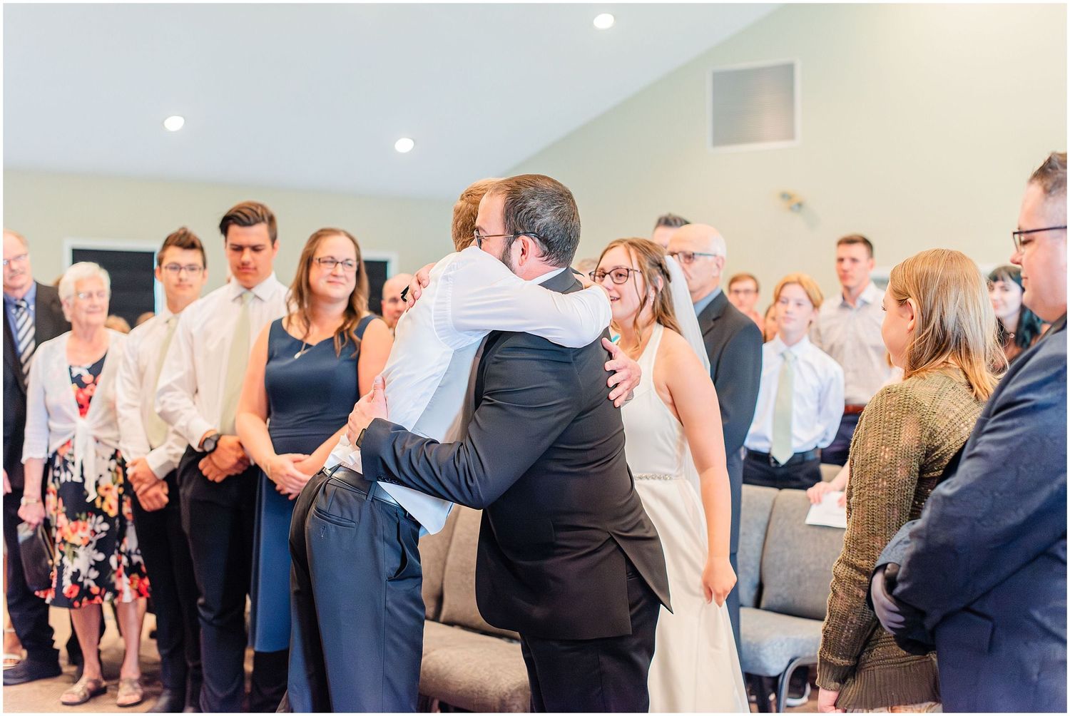 Bride and groom share a warm hug with guests during an intimate indoor wedding ceremony.