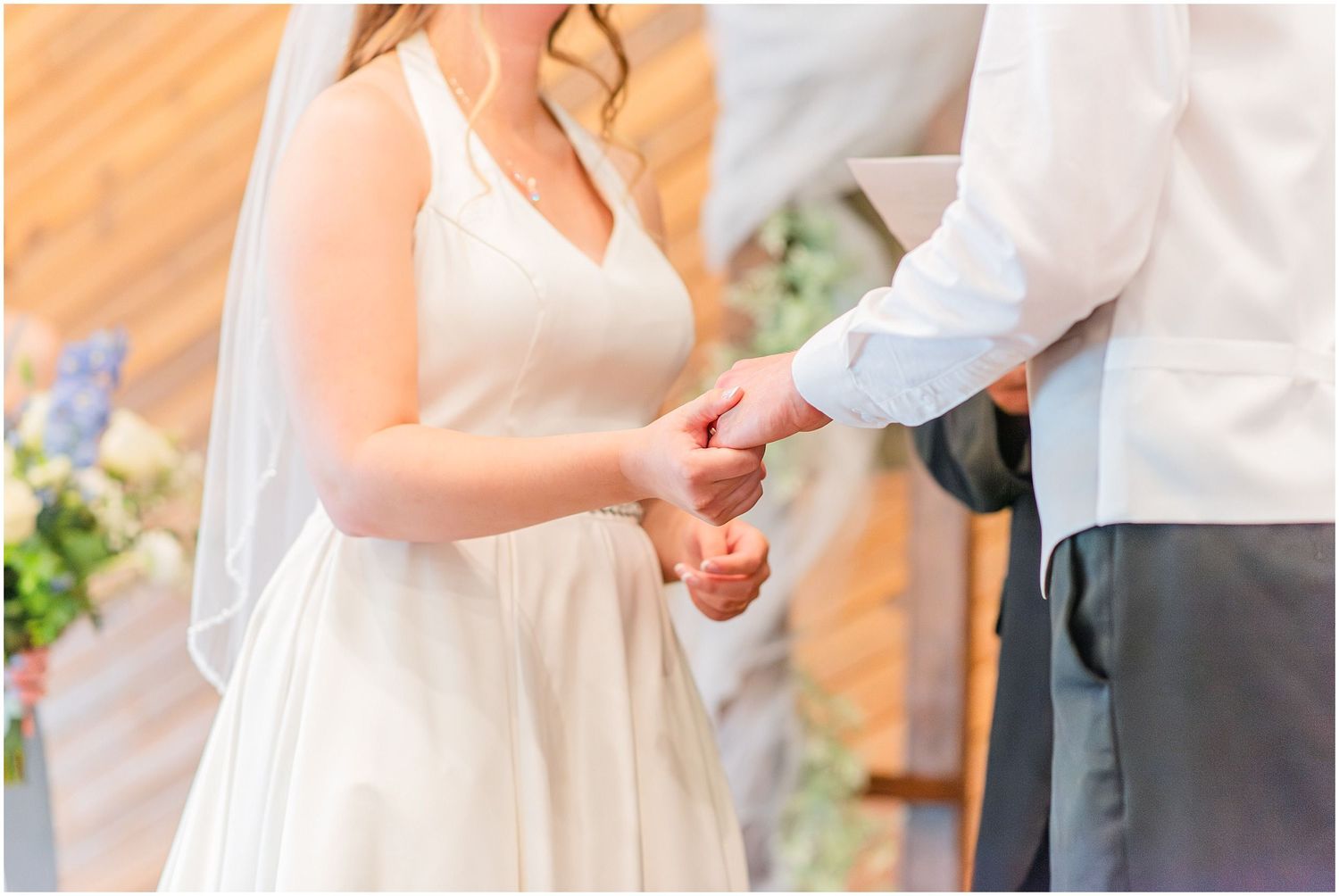 Close-up of bride and groom holding hands during wedding ring exchange ceremony.