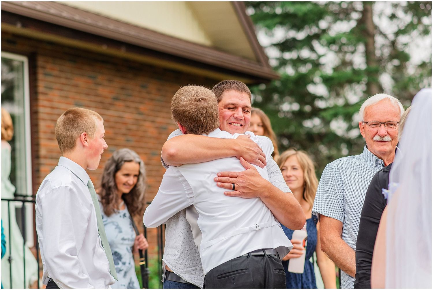 Two men sharing a warm hug at an outdoor wedding reception celebration.