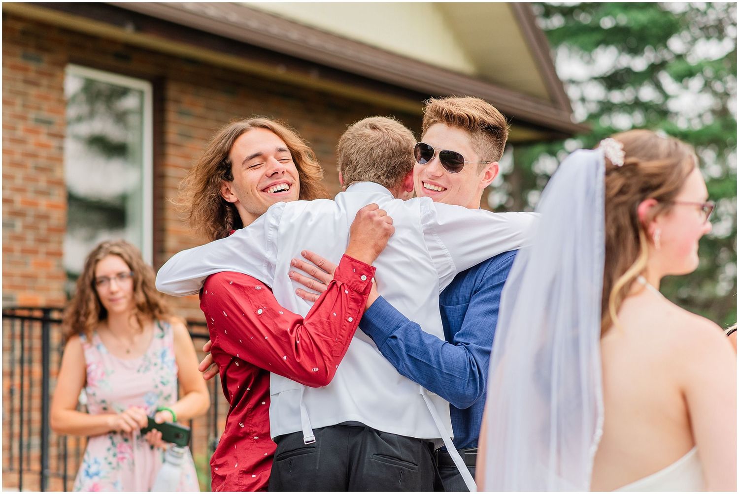 Groomsmen share joyful hugs outside while the bride stands nearby in her veil.