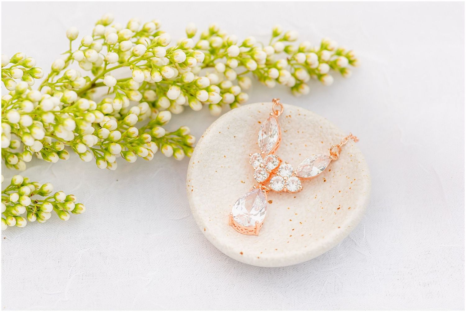Rose gold butterfly earrings with sparkling crystals displayed on a ceramic dish beside delicate white flowers.