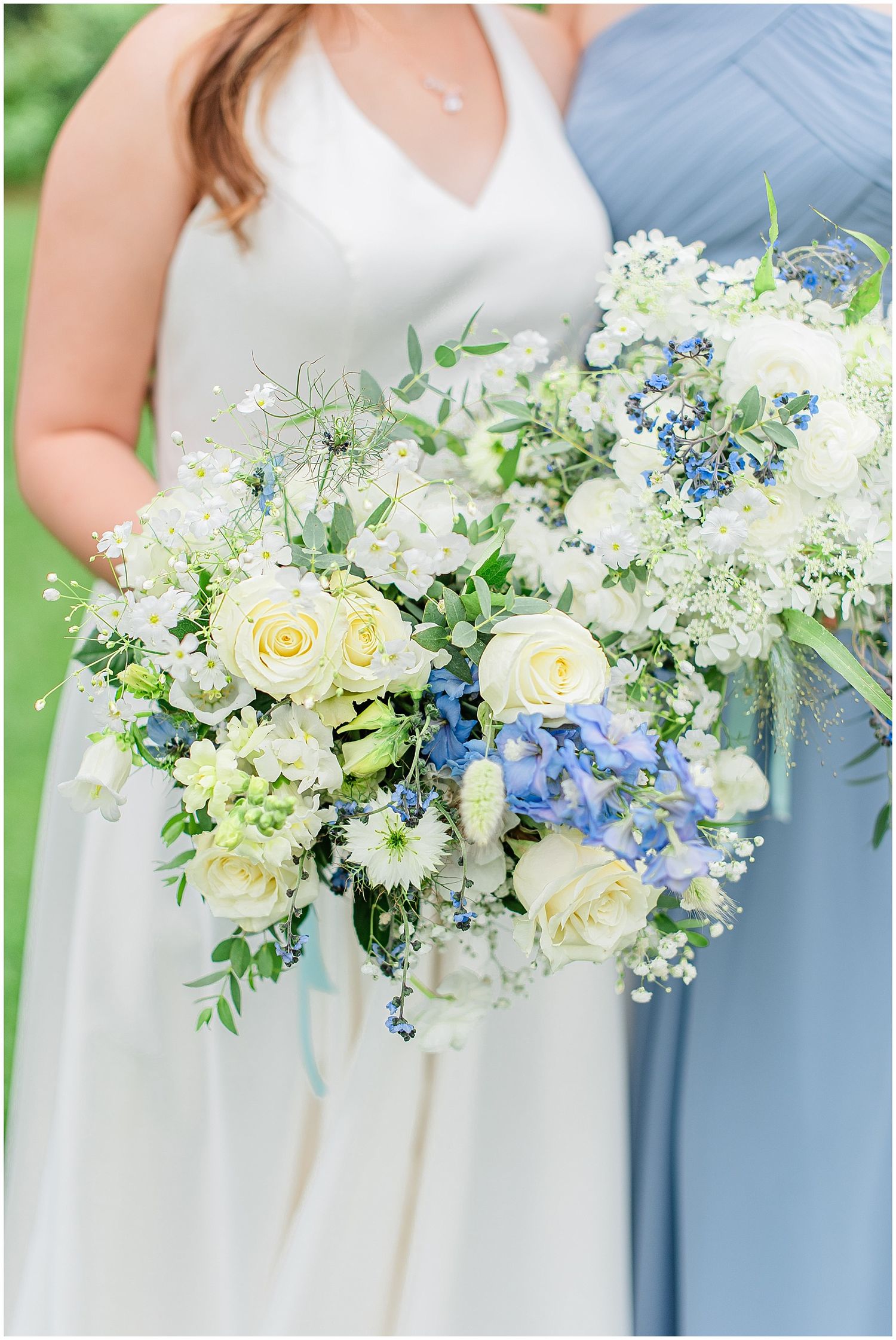 Bride and bridesmaid hold lush white and blue floral bouquets with roses and hydrangeas.