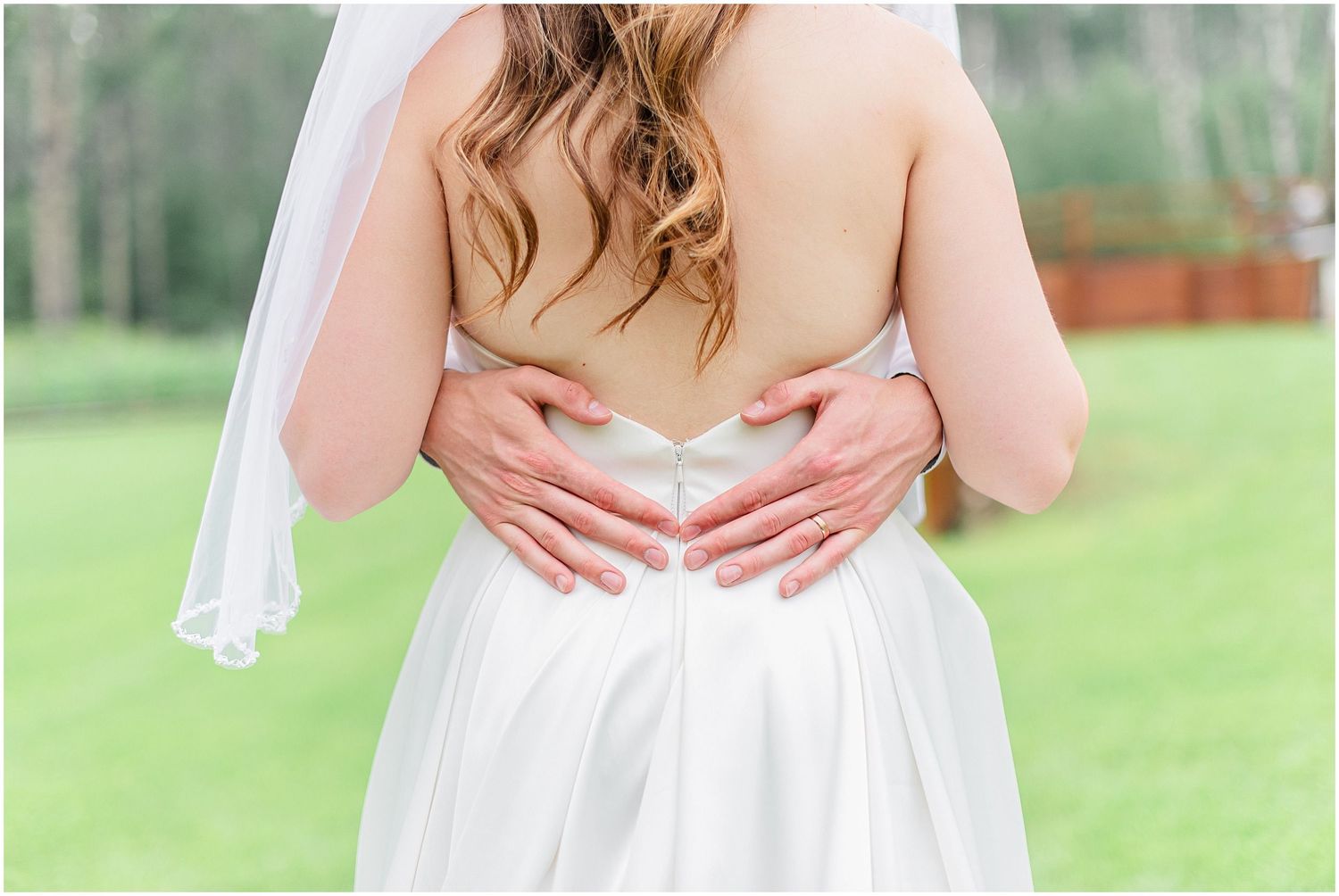 Close-up of bride's open back wedding dress with groom's hands resting on her waist.