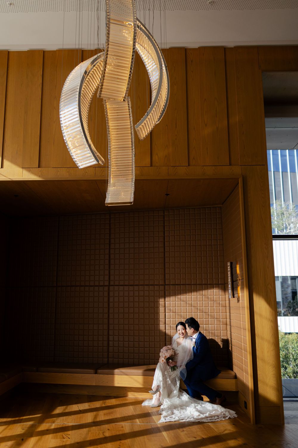 Wedding couple sharing an intimate moment in a warmly lit wooden interior beneath a modern spiral chandelier.