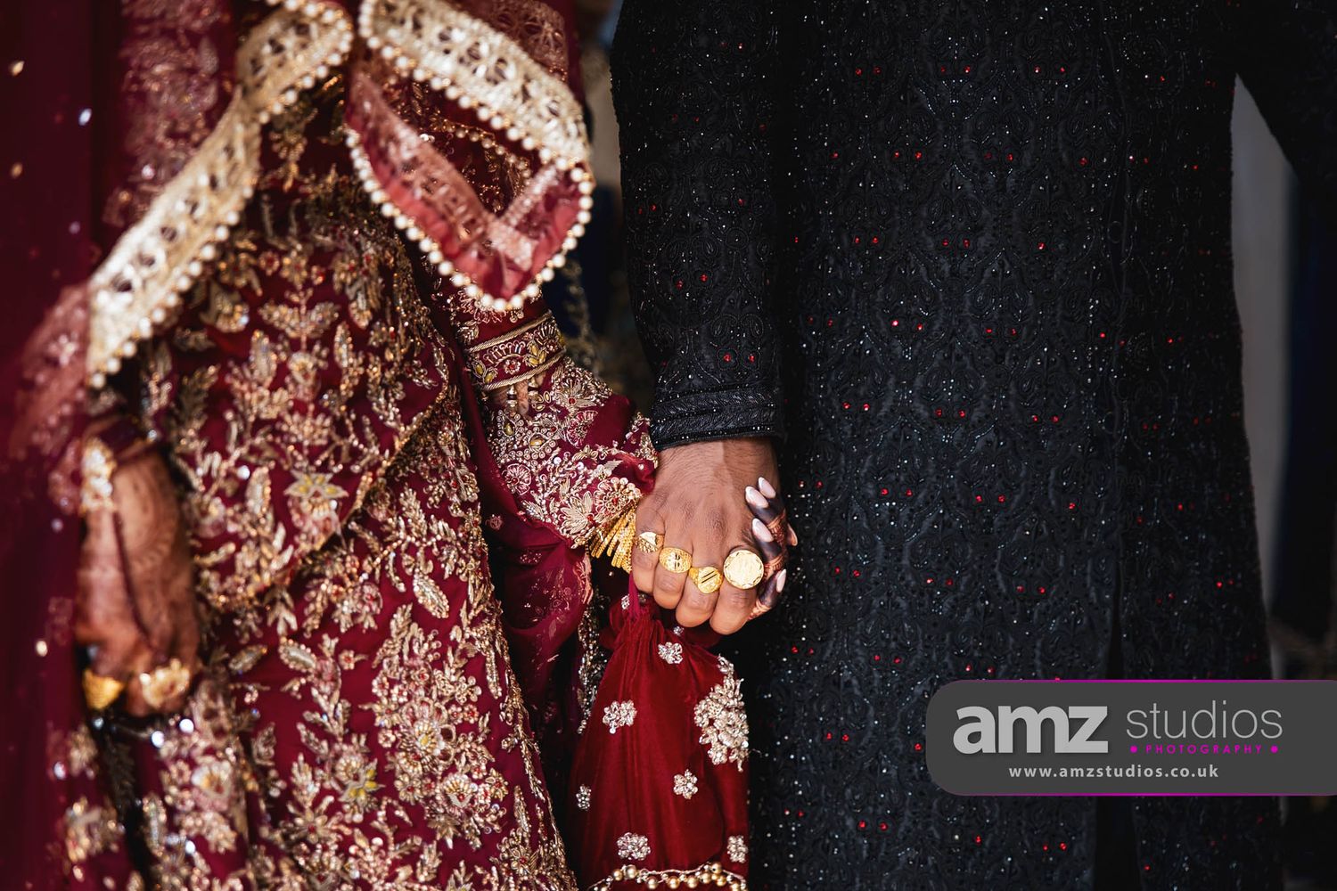 South Asian bride and groom in traditional wedding attire holding hands, bride wearing red and gold embroidered lehenga.