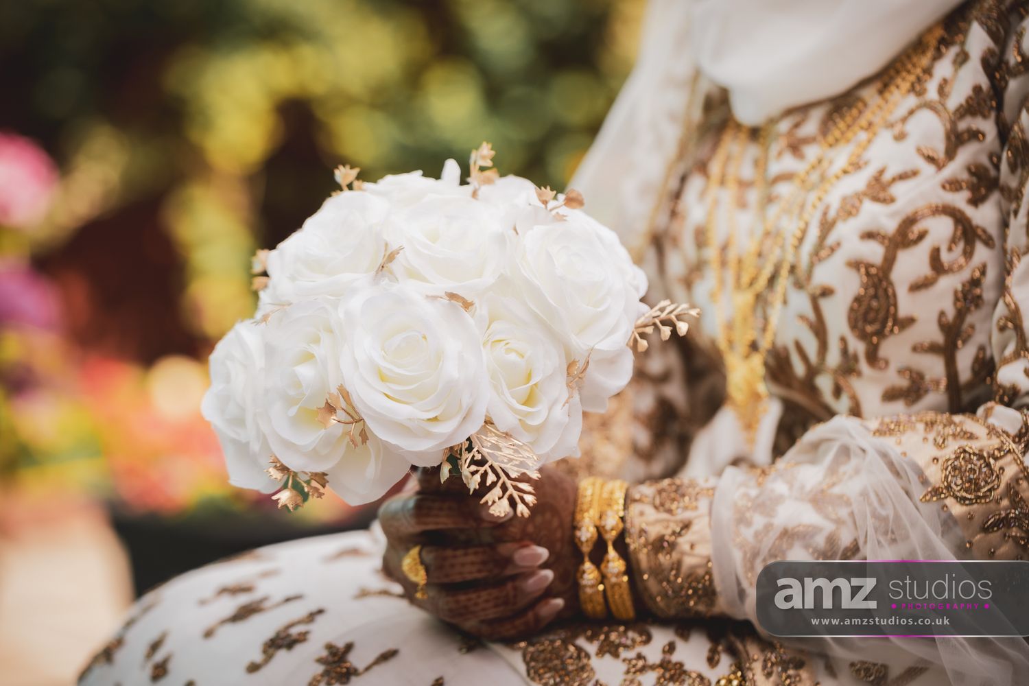 Bride in ornate gold embroidered dress holding elegant white rose bouquet with gold accents, showcasing intricate mehndi henna hands.