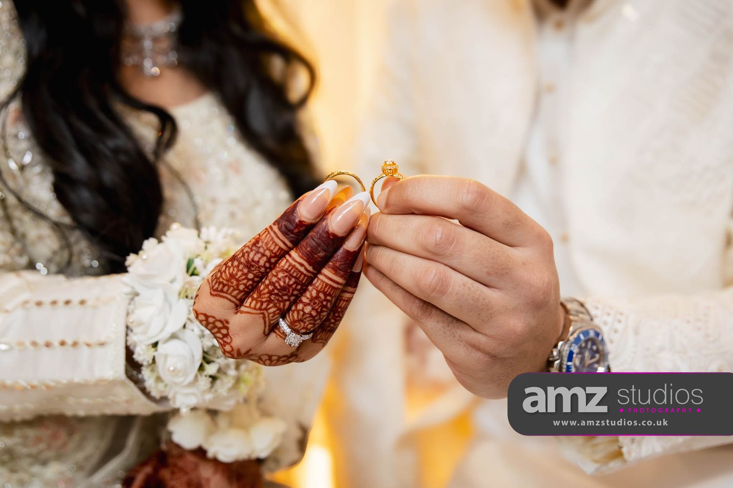 Close-up of a South Asian bride with mehndi-covered hands receiving a gold ring during a traditional wedding ceremony.