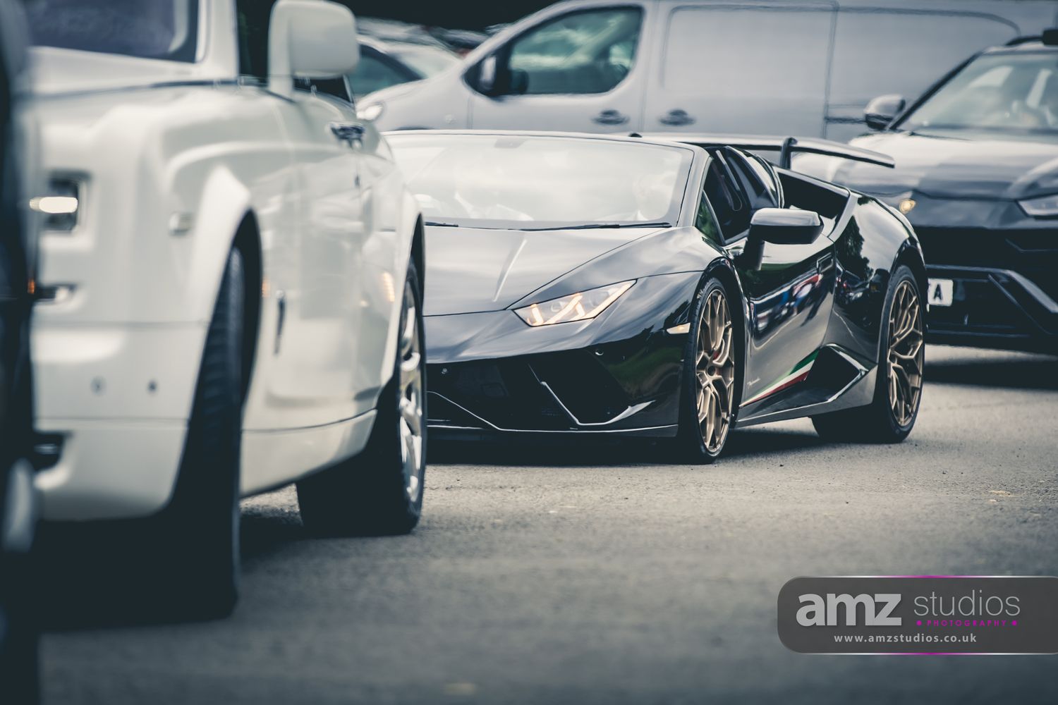 Black Lamborghini Huracan supercar parked between luxury vehicles including a Rolls-Royce, shot by AMZ Studios.