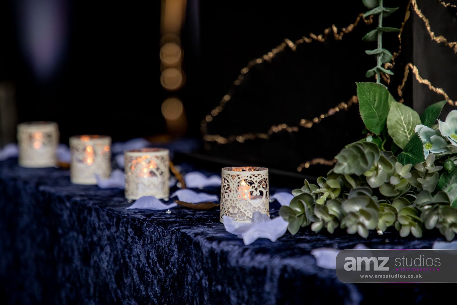 Elegant wedding table decor with ornate white candle holders and lush greenery on a navy blue velvet tablecloth.