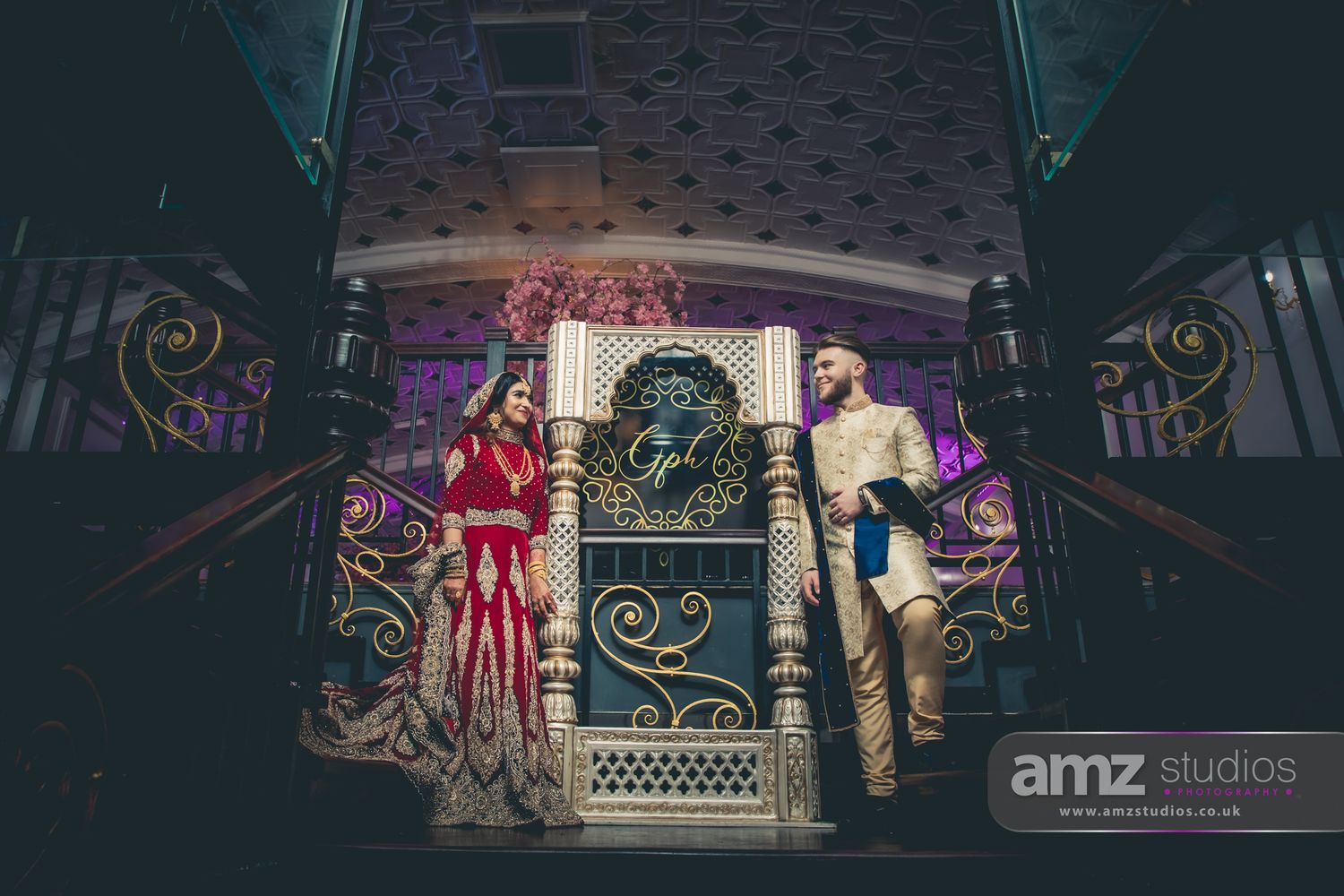 Couple in traditional Indian wedding attire posing on an ornate stage at a South Asian wedding reception.