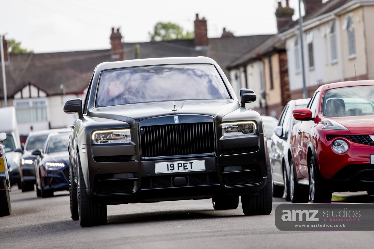 Black Rolls-Royce Cullinan SUV with license plate 19 PET driving down a residential street.