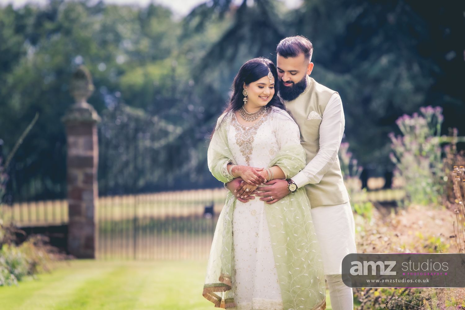 South Asian couple in traditional attire embracing in a lush garden setting during their wedding celebration.