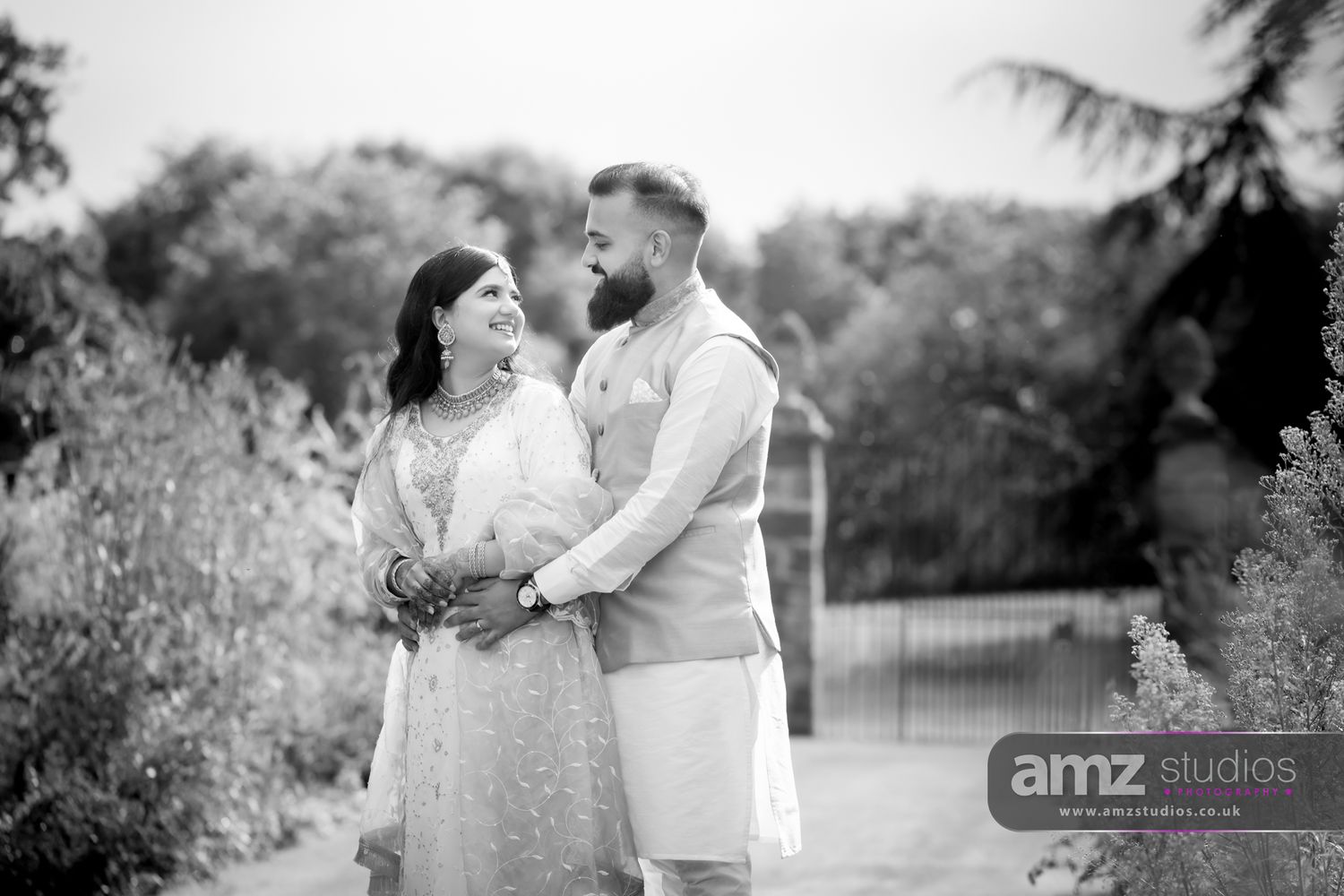 Black and white photo of a South Asian couple in traditional attire sharing a romantic moment outdoors at their wedding.