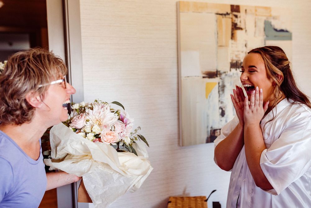 Man surprises woman with a bouquet of pink and white flowers, as she reacts with joy and excitement.