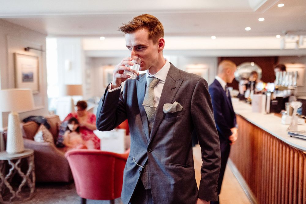 Elegant man in grey suit drinking water at a hotel bar reception area.