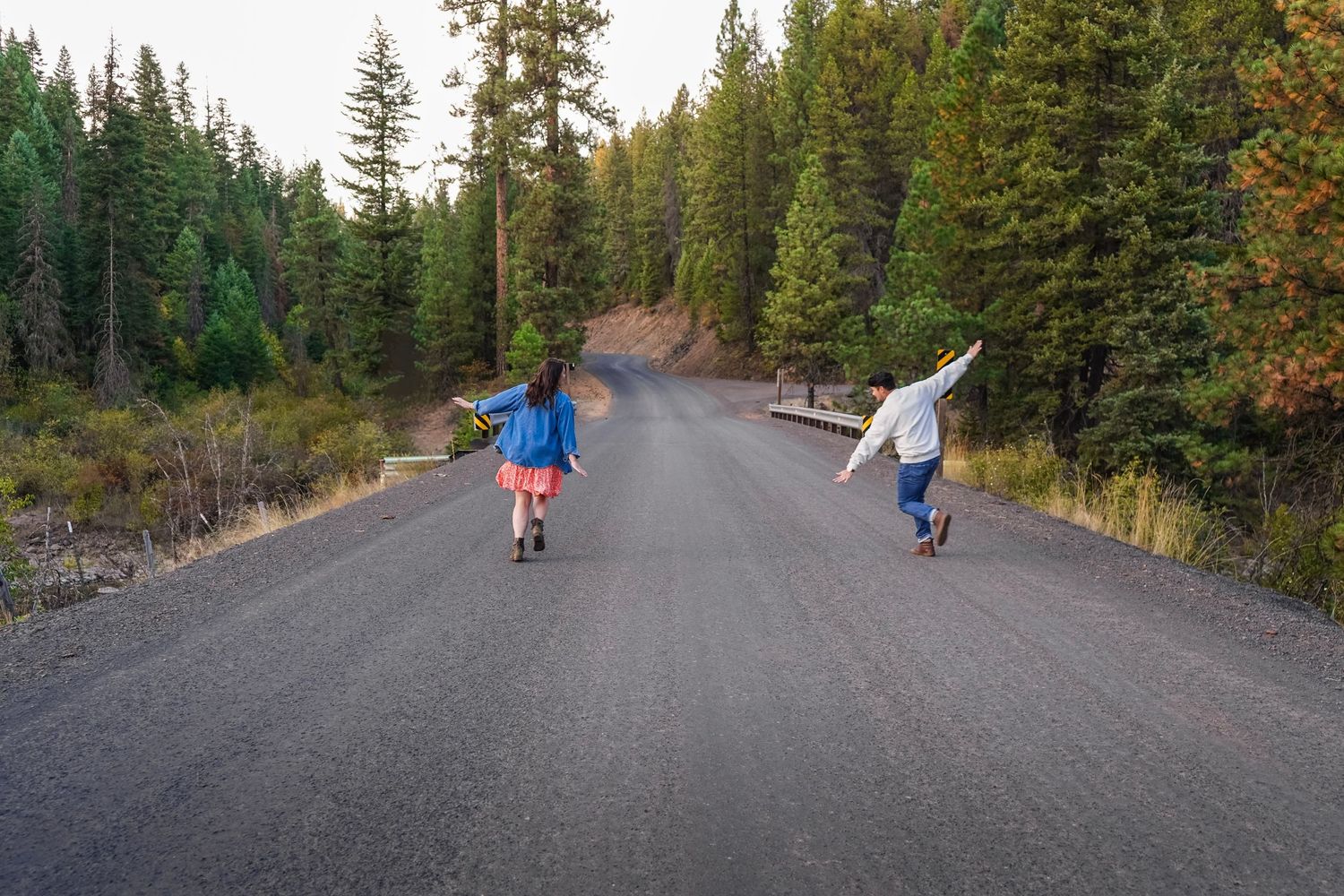 Two children skateboarding down a tree-lined road with arms outstretched, enjoying a sunny day outdoors.