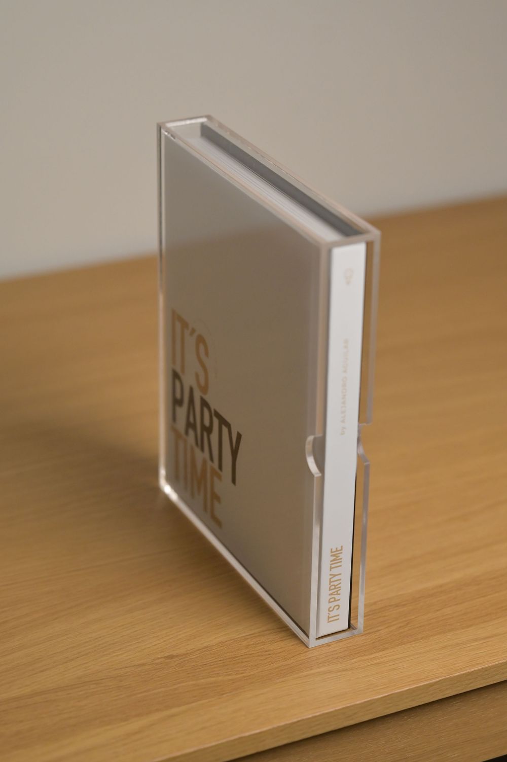 Clear acrylic box containing an Its Party Time photo book standing upright on a wooden surface.