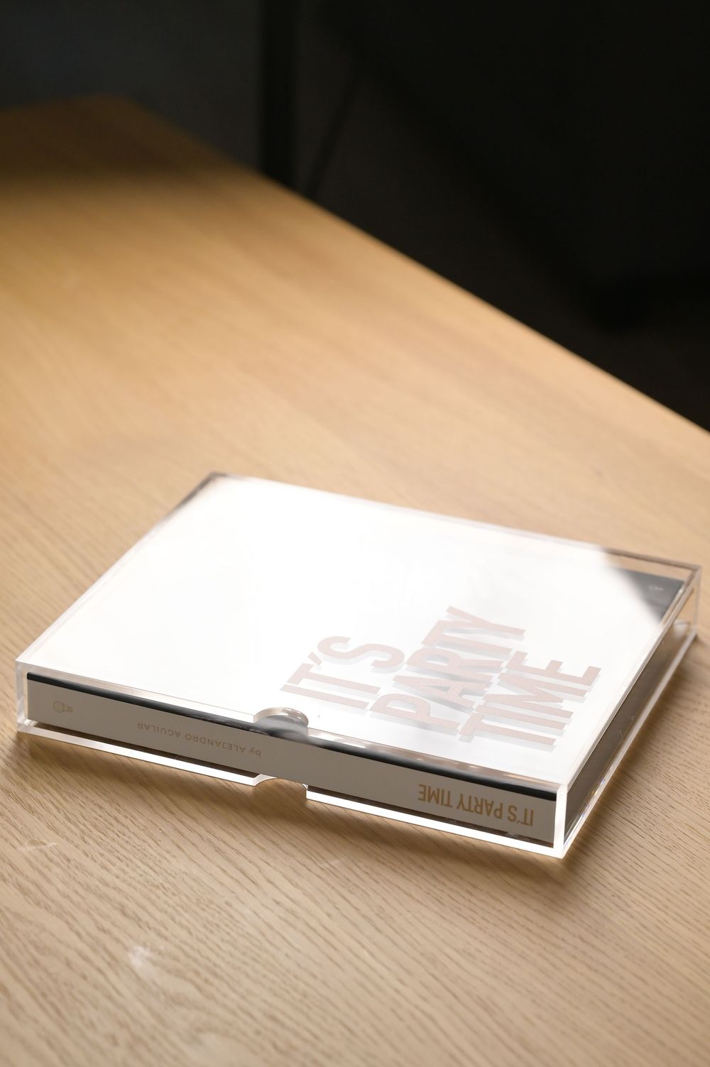 White hardcover Its Party Time photo book stored in a clear acrylic display case on desk.