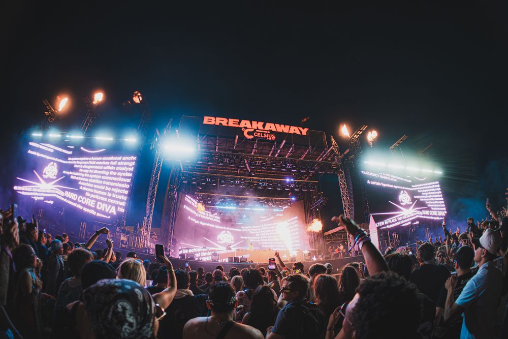 Breakaway music festival night concert with massive LED stage, colorful lights, and large crowd of fans.