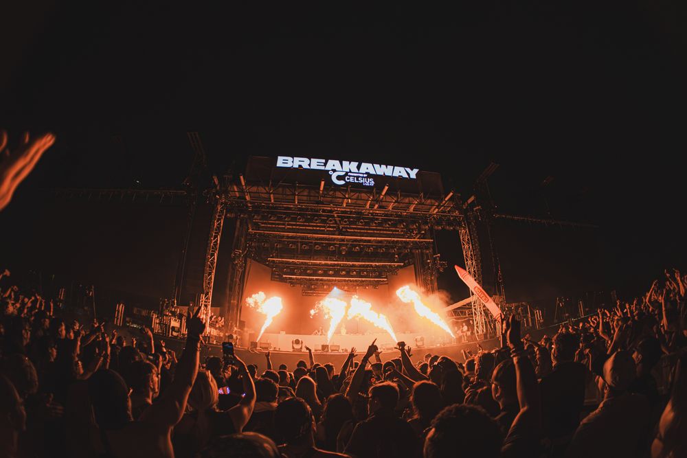 Breakaway Music Festival crowd cheering before a lit stage with orange lights at night.