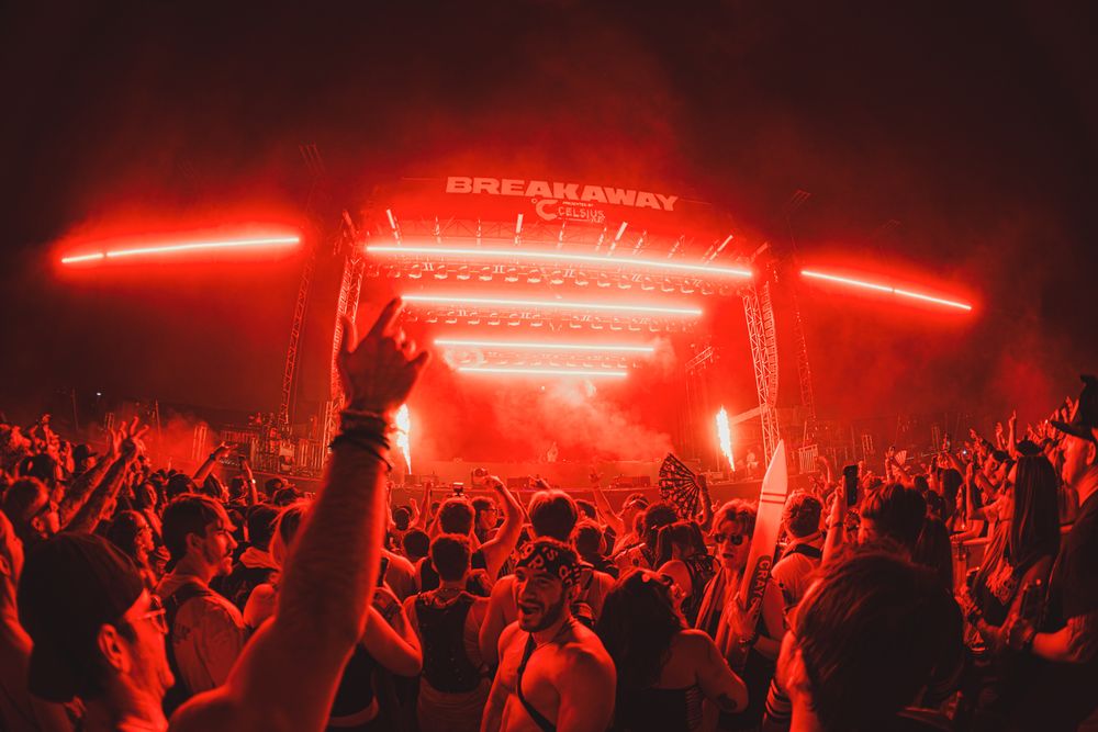 Crowd at Breakaway Music Festival bathed in red lights with hands raised toward illuminated stage.